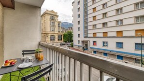 A balcony with a table set for dining, overlooking a street with buildings and a mountain in the background. - Victoria CHIC Studio - Downtown - Balcony with Mountain Views (Aix les Bains)