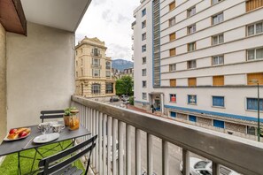 En balkon med et spisebord, der udover en gade med bygninger og et bjerg i baggrunden.