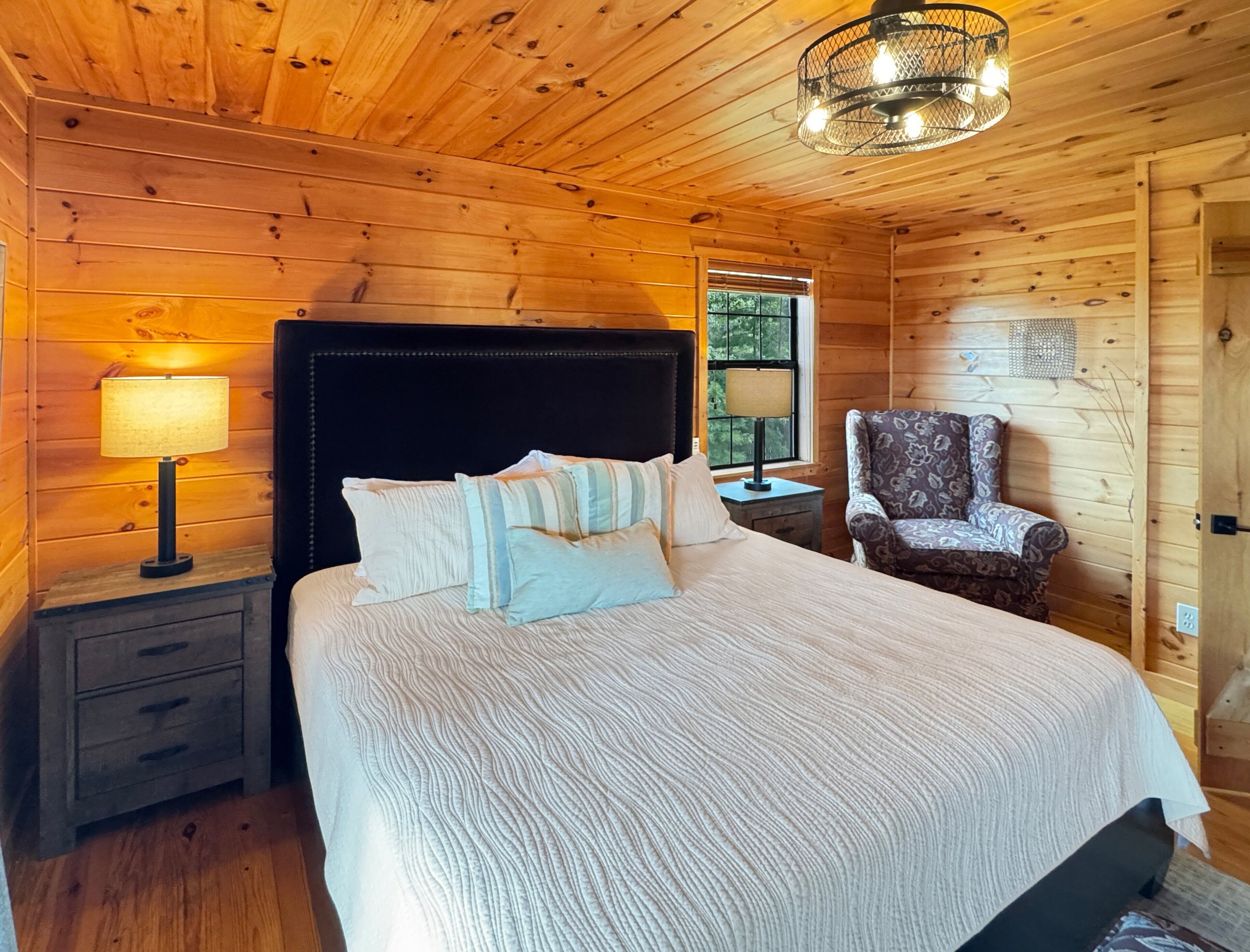 A wooden cabin bedroom with a bed, nightstands, a chair, and a chandelier.