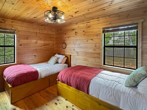 Eine Hütte mit zwei Holzbetten, einer Pendelleuchte und Fenstern mit Blick ins Freie.
