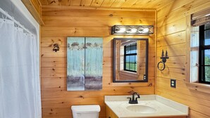 A wooden cabin bathroom with a toilet, sink, and cabinets. - Southwind Ridge - Mountain View | Screened porch | Fireplace (Morganton)