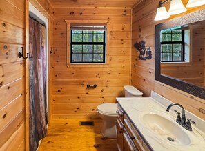 Une salle de bain rustique, aménagée dans une cabane en bois, avec des toilettes, un lavabo et une fenêtre.