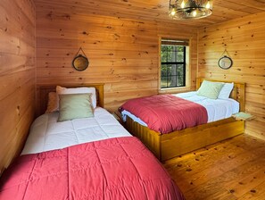A cabin room with two wooden beds, a window, and a hanging light fixture. - Southwind Ridge - Mountain View | Screened porch | Fireplace (Morganton)