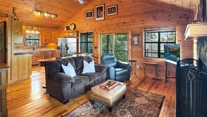 A cabin interior with a wooden ceiling, a sofa, a leather chair, a dining table, and a kitchen area. - Southwind Ridge - Mountain View | Screened porch | Fireplace (Morganton)