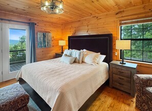 Une chambre à coucher aux murs lambrissés, avec un grand lit, deux tables de chevet, une petite table et une fenêtre donnant sur l’extérieur.