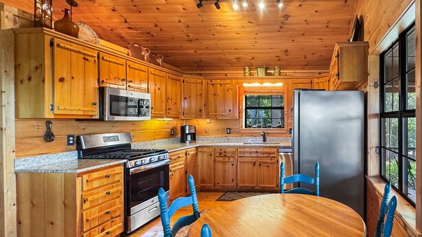 A wooden cabin kitchen with a central island, wooden cabinets, a stove, microwave, refrigerator, and a dining table with chairs. - Southwind Ridge - Mountain View | Screened porch | Fireplace (Morganton)