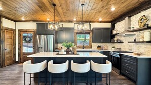 A modern kitchen with a central island, bar stools, and a stone backsplash. - Hope Ridge Manor - Pet Friendly | Firepit | Hot Tub | Game Room (Blue Ridge)