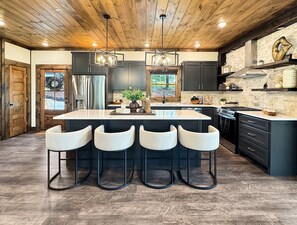 A modern kitchen with a central island, bar stools, and a stone backsplash. - Hope Ridge Manor - Pet Friendly | Firepit | Hot Tub | Game Room (Blue Ridge)