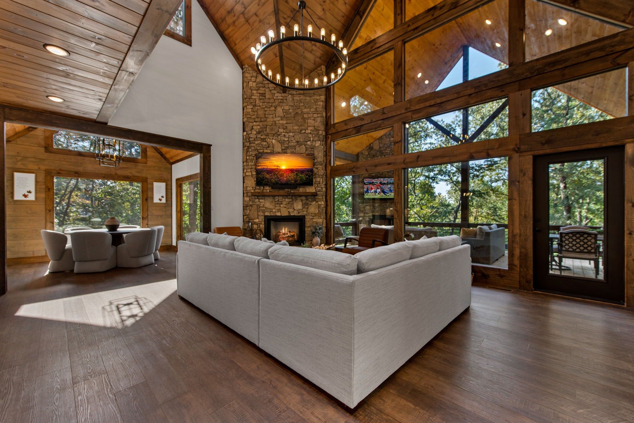 A spacious living room with a large sectional sofa, a stone fireplace, and large windows offering views of the outdoors.