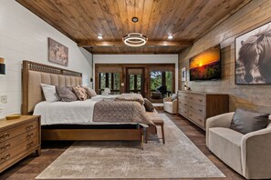 A bedroom with a wooden ceiling, a bed with multiple pillows, a dresser, and a chair. - Hope Ridge Manor - Pet Friendly | Firepit | Hot Tub | Game Room (Blue Ridge)