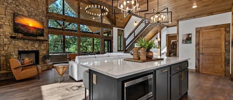 Una cocina amplia con una isla grande, una chimenea de piedra y vistas al exterior a través de amplios ventanales.