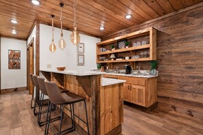 A kitchen with wooden cabinets, a marble countertop, and hanging pendant lights. - Hope Ridge Manor - Pet Friendly | Firepit | Hot Tub | Game Room (Blue Ridge)
