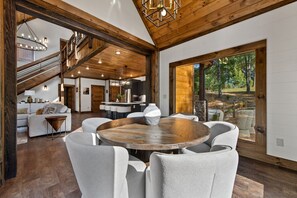 A spacious living area with a round wooden table, grey upholstered chairs, and a large window offering a view of the outdoors. - Hope Ridge Manor - Pet Friendly | Firepit | Hot Tub | Game Room (Blue Ridge)