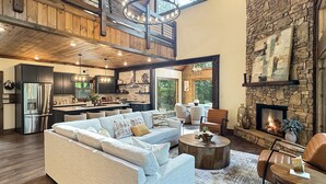 A spacious living area with a modern sofa, a fireplace, and a kitchen in the background. - Hope Ridge Manor - Pet Friendly | Firepit | Hot Tub | Game Room (Blue Ridge)