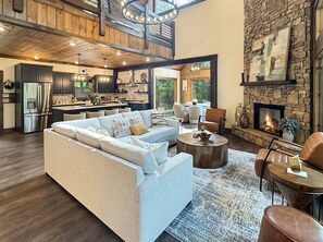 A spacious living area with a modern sofa, a fireplace, and a kitchen in the background. - Hope Ridge Manor - Pet Friendly | Firepit | Hot Tub | Game Room (Blue Ridge)