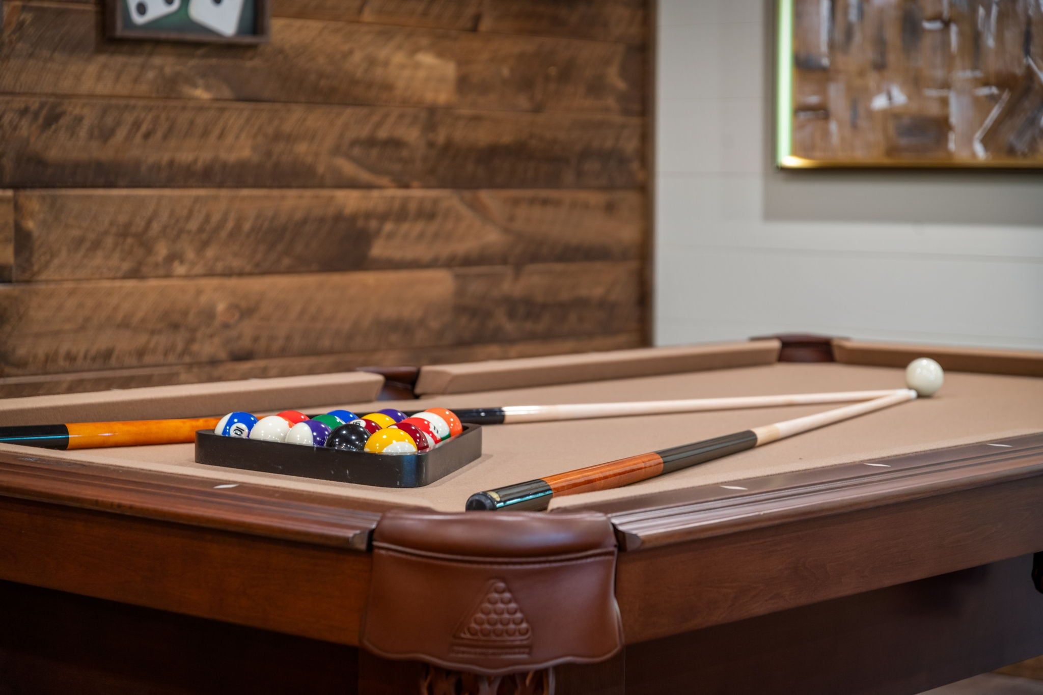 A pool table with balls and cues, a wooden wall, and a framed picture.