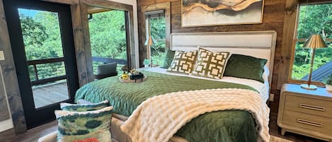 Une chambre à coucher avec un grand lit, une table de chevet, une chaise et une fenêtre donnant sur un paysage verdoyant.