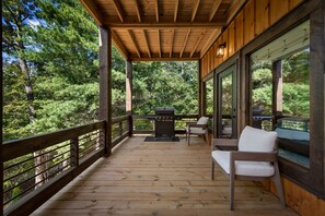 A wooden deck with a grill, chairs, and a view of a forest. - Hope Ridge Manor - Pet Friendly | Firepit | Hot Tub | Game Room (Blue Ridge)