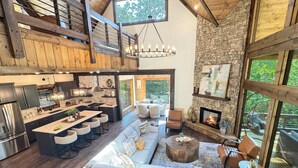 A spacious living area with a large sofa, a dining table with bar stools, and a stone fireplace. - Hope Ridge Manor - Pet Friendly | Firepit | Hot Tub | Game Room (Blue Ridge)
