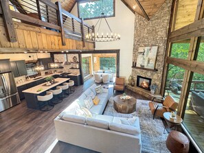 A spacious living area with a large sofa, a dining table with bar stools, and a stone fireplace. - Hope Ridge Manor - Pet Friendly | Firepit | Hot Tub | Game Room (Blue Ridge)