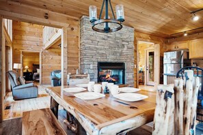A wooden interior with a stone fireplace, a dining table set for four, and a staircase leading to an upper level. - Gatlinburg: 4 King Ensuites, Hot Tub, Pool Table (Gatlinburg)