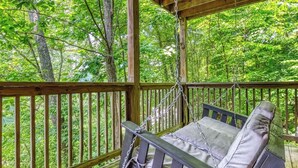 Un terrazzo in legno con una sedia a dondolo e vista su una foresta.