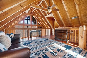 A spacious attic room with a sloped ceiling, a ceiling fan, a large window, a wooden dresser, and a patterned rug. - Gatlinburg: 4 King Ensuites, Hot Tub, Pool Table (Gatlinburg)