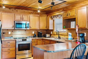 A kitchen with wooden cabinets, a stainless steel refrigerator, a microwave, an oven, a coffee maker, and a roll of paper towels. - Gatlinburg: 4 King Ensuites, Hot Tub, Pool Table (Gatlinburg)