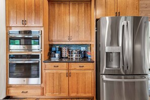 A kitchen with wooden cabinets, stainless steel appliances including a refrigerator, and a coffee maker. - R&R Chalet | Ski View | Hot Tub | Theater | Sauna (McGaheysville)