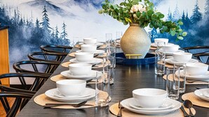 Una mesa de comedor dispuesta con cuencos y vasos blancos, rodeada de sillas, con un mural de un bosque al fondo.