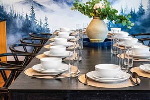 A dining table set with white bowls and glasses, surrounded by chairs, with a forest mural in the background. - R&R Chalet | Ski View | Hot Tub | Theater | Sauna (McGaheysville)