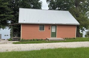 A small, single-story cabin with a metal roof, a green door, and a small porch.