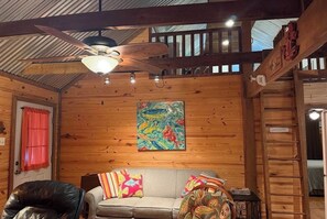 A wooden interior with a ceiling fan, a sofa with colorful cushions, and a painting on the wall.