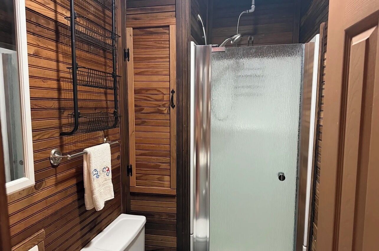 A bathroom with a wooden wall, a white bathtub, a glass shower enclosure, and a towel rack.