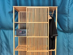 A wooden wardrobe with multiple shelves and a hanging rod, containing clothes and a black electronic device.