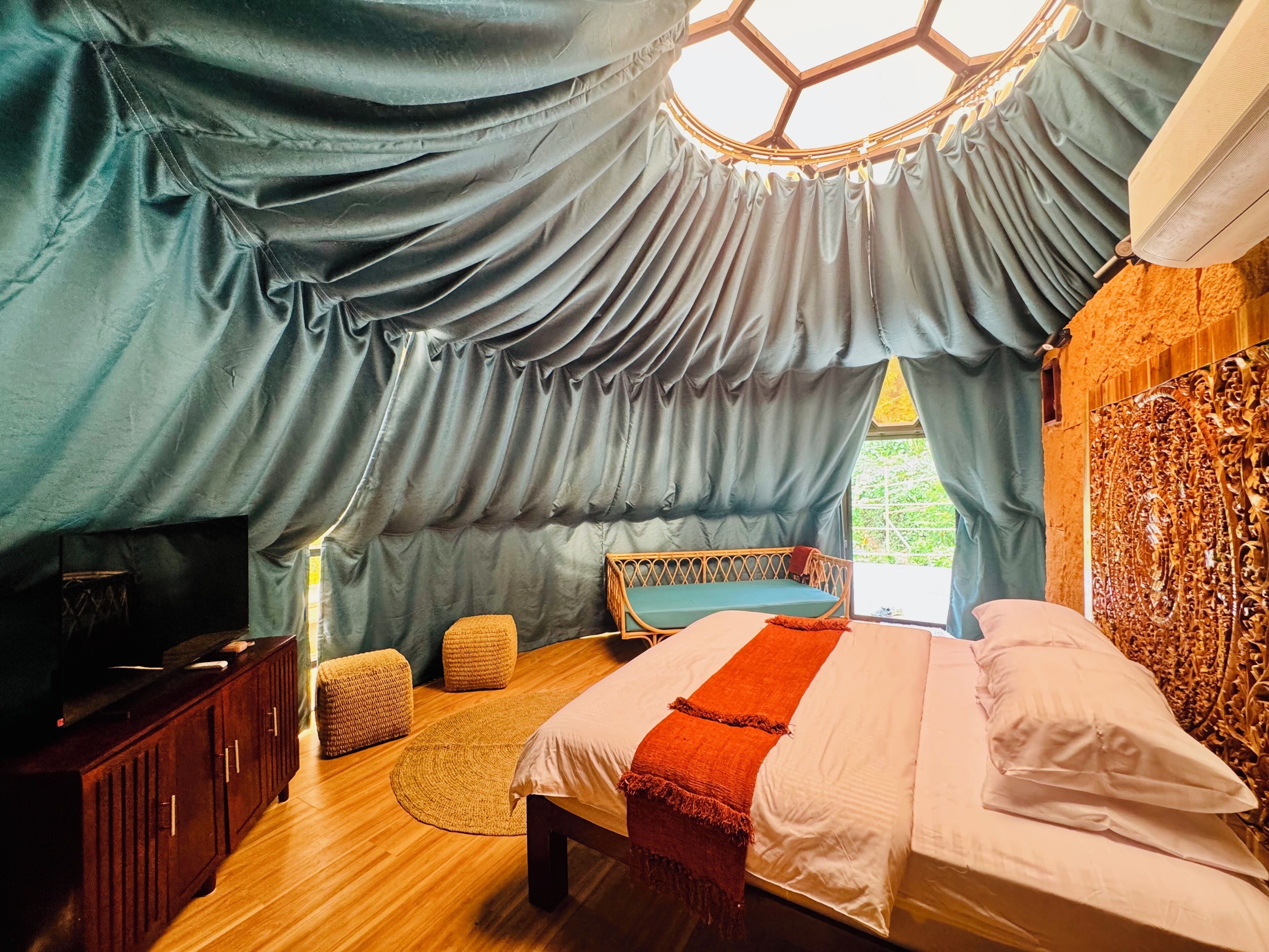 Une chambre à coucher comprenant un lit, une armoire en bois, un coin salon avec des coussins et une fenêtre avec des rideaux.