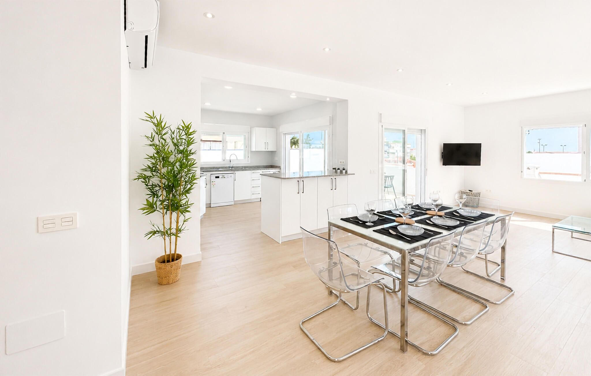 A modern kitchen with white cabinets, a dining area with a glass table and chairs, and a large window providing natural light.