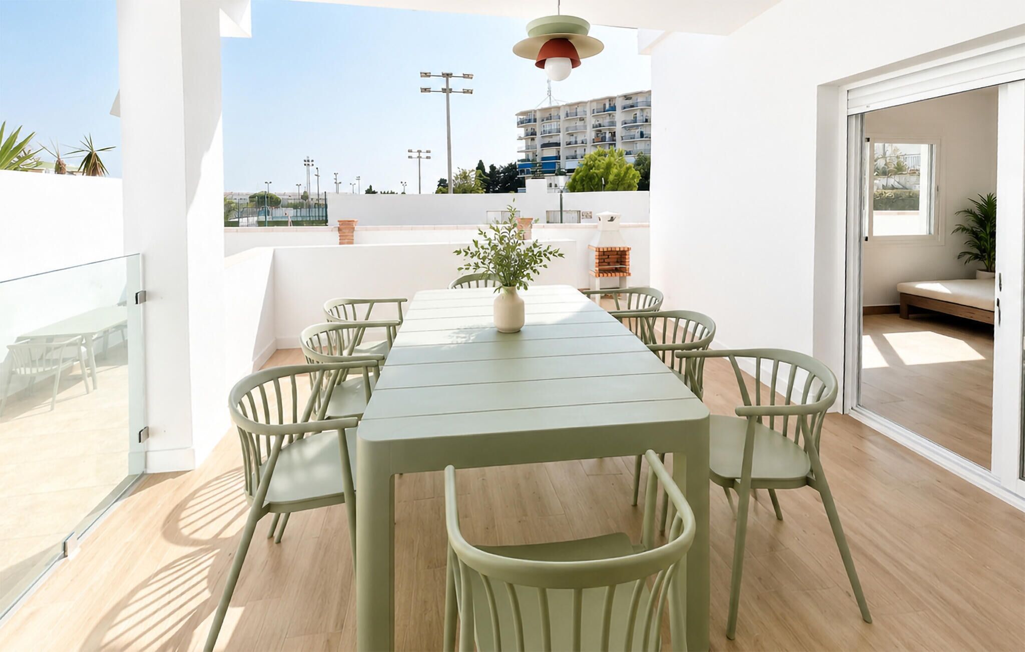 Een eetgedeelte met een tafel, stoelen, een plant in pot en een gebouw op de achtergrond.