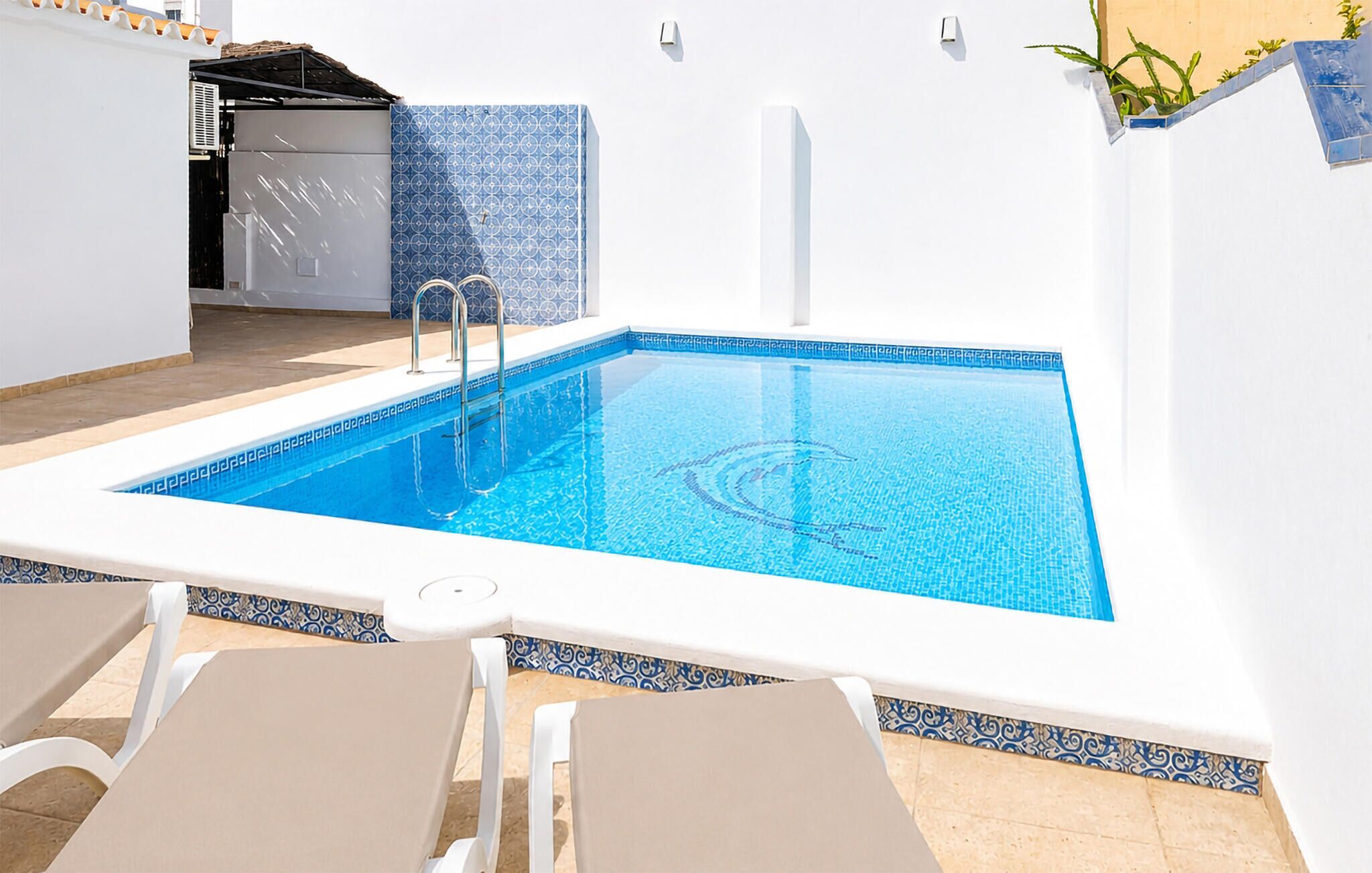 Una piscina rectangular amb superfície d'aigua blava i transparent, envoltada de parets blanques i una vora de rajola.