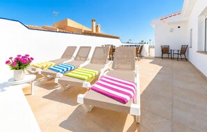 Eine Dachterrasse mit Liegestühlen, einem Tisch mit Stühlen und einem Blumentopf.