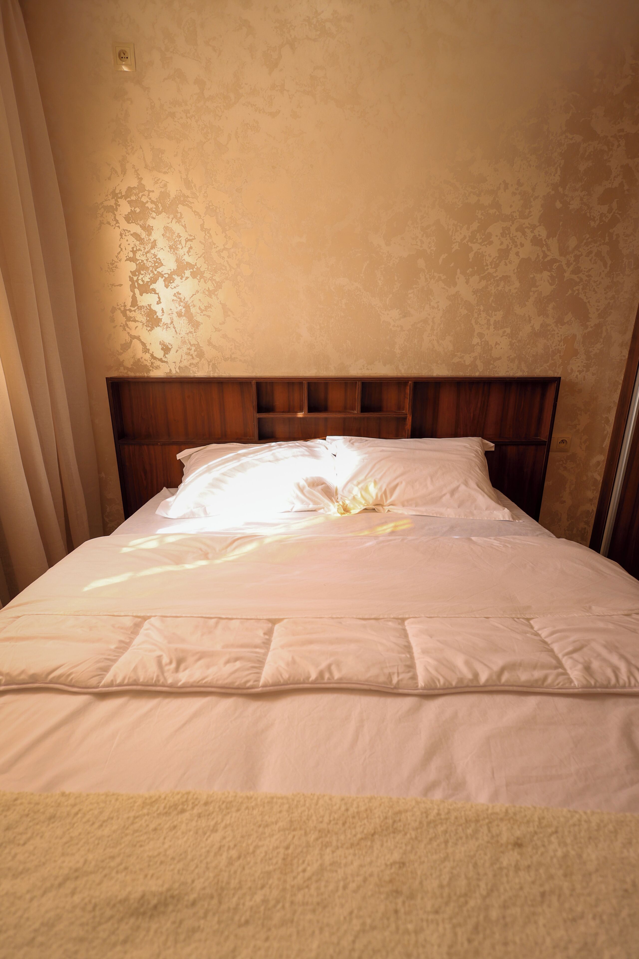 Ein ordentlich bezogenes Bett mit einem hölzernen Kopfteil, einer weißen Daunendecke und Kissen.