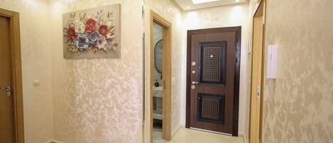 A hallway with a decorative floral wall art, a wooden door with a grid pattern, and a tiled floor.