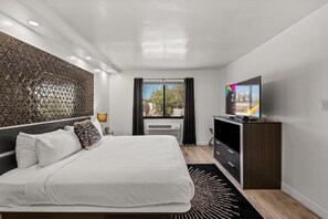 A modern hotel room with a large bed, a flat-screen TV, a decorative wall panel, and a view of the outdoors. - Cozy 1-bedroom hotel in charming Albuquerque with AC (Albuquerque)