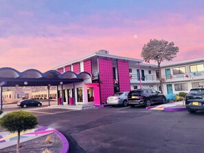 A building with a distinctive pink facade, a covered entrance, and a parking area with several cars. - Cozy 1-bedroom hotel in charming Albuquerque with AC (Albuquerque)