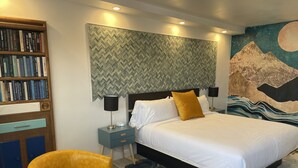 Un dormitorio moderno con una cama grande, una mesita de noche con lámpara, una estantería y un mural decorativo en la pared.