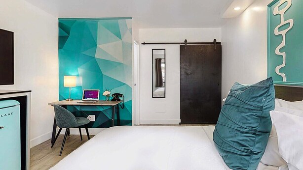 Una habitación de hotel con una cama, un escritorio con una computadora, una silla y un mini bar.