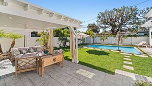 A backyard with a pool, a covered patio area, and a lawn. - Spacious 4-bedroom house in charming Toluca Woods (Los Angeles)