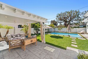 Ein Garten mit Schwimmbad, einer überdachten Terrasse und einem Rasen.