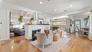 A spacious living area with a fireplace, seating, and a view to the kitchen. - Spacious 4-bedroom house in charming Toluca Woods (Los Angeles)
