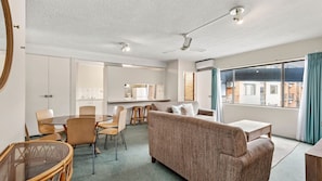 Ein modernes Wohnzimmer mit einer Couch, Sesseln, einem Esstisch und einer Küchenzeile.